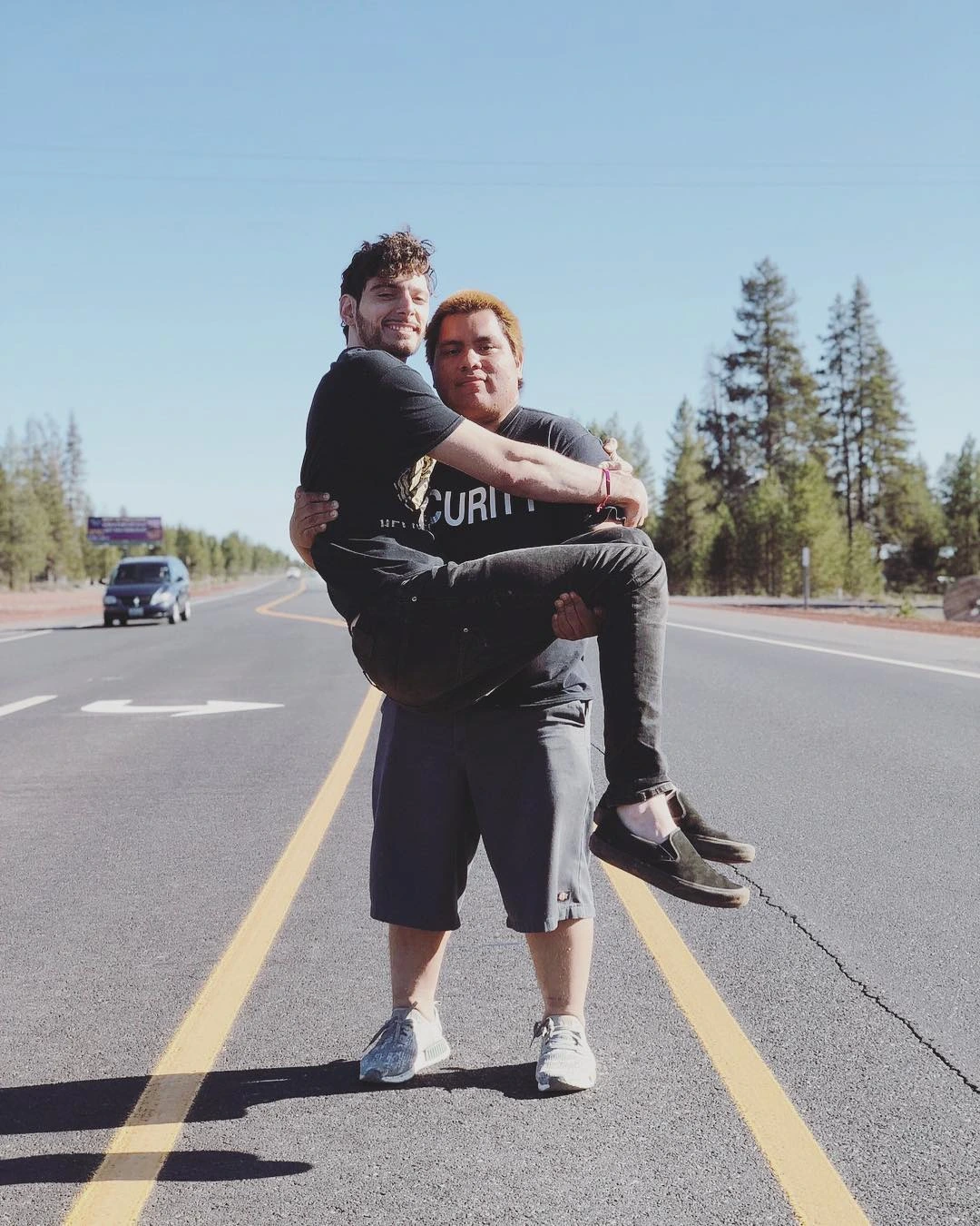 Paul Denino (Ice Poseidon) standing outdoors on a road, smiling while carrying another person.