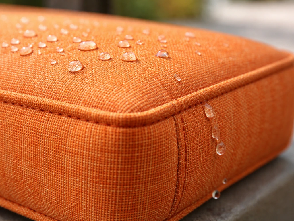 Close-up of vibrant solution-dyed acrylic cushion fabric with visible weave and water beading on stitching.