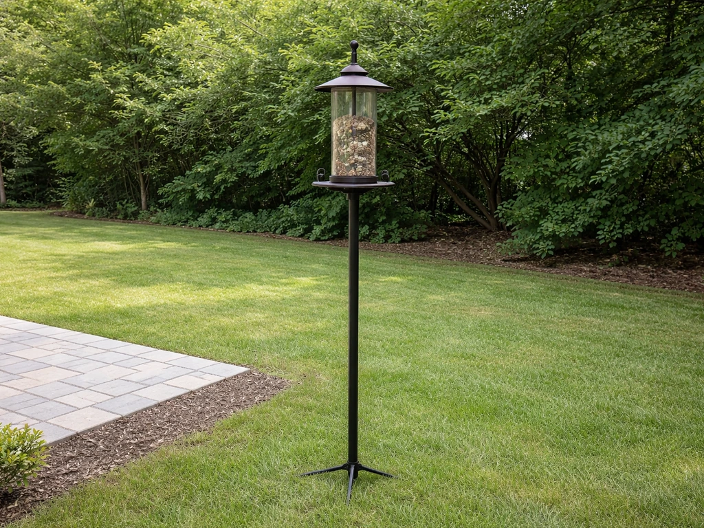 Side view of a bird feeder on a pole set away from nearby shrubs in a quiet yard