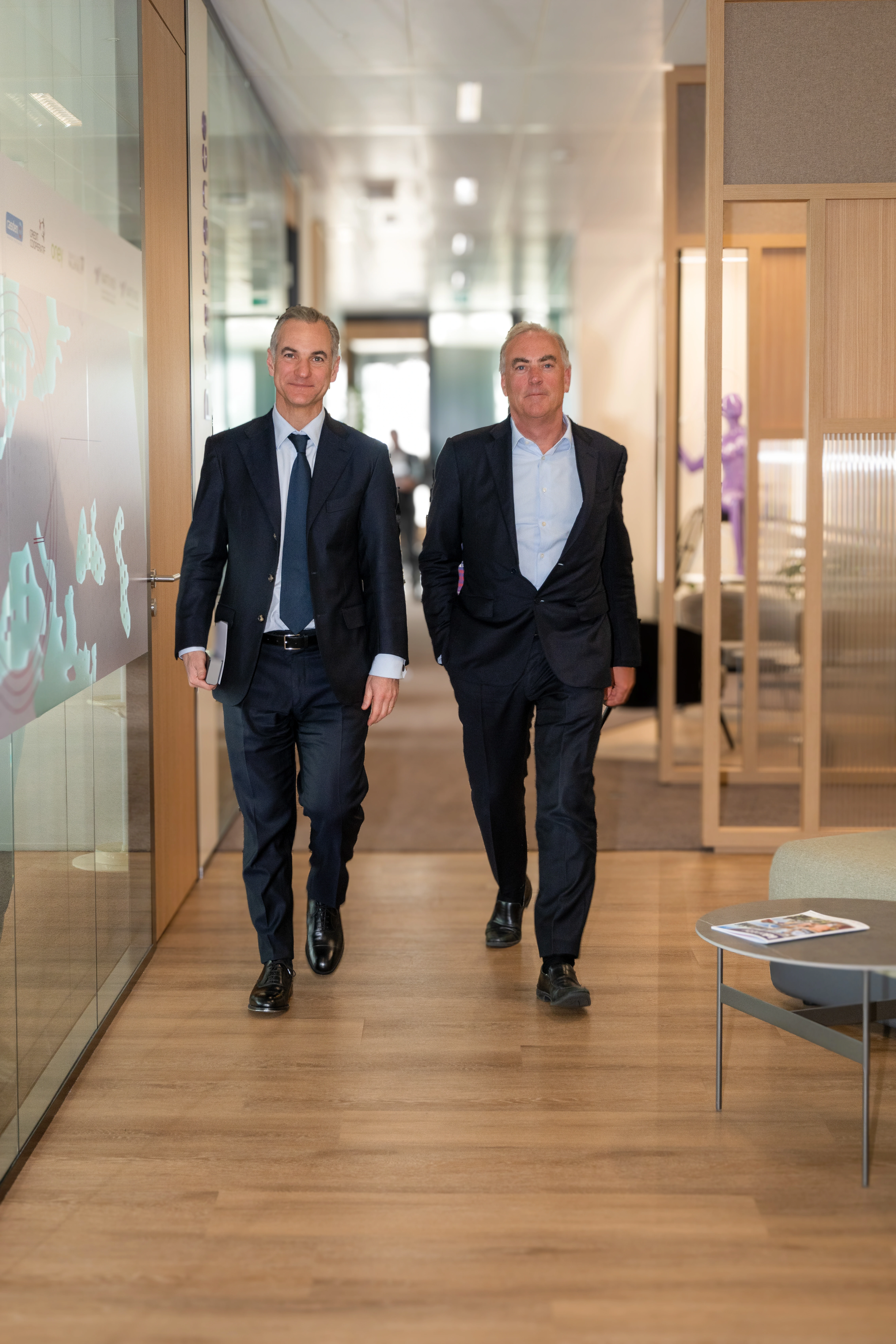 Two businessmen walking through a modern office corridor, one of whom is Nicolas Namias.