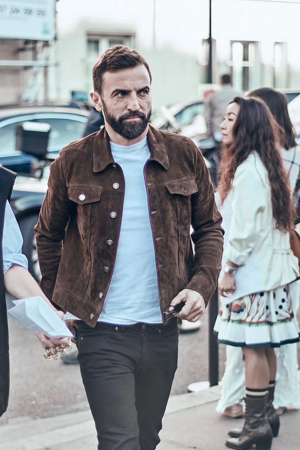 Nicolas Ghesquière walking outdoors at Paris Fashion Week, wearing a brown jacket over a white shirt