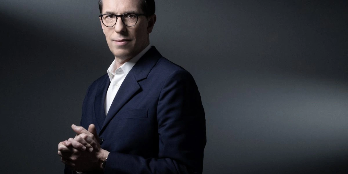 Portrait of Nicolas Hieronimus in a dark suit and glasses against a gray background.