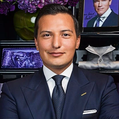 Portrait of Nicolas Bijan Pakzad in a suit, standing in front of fashion display imagery