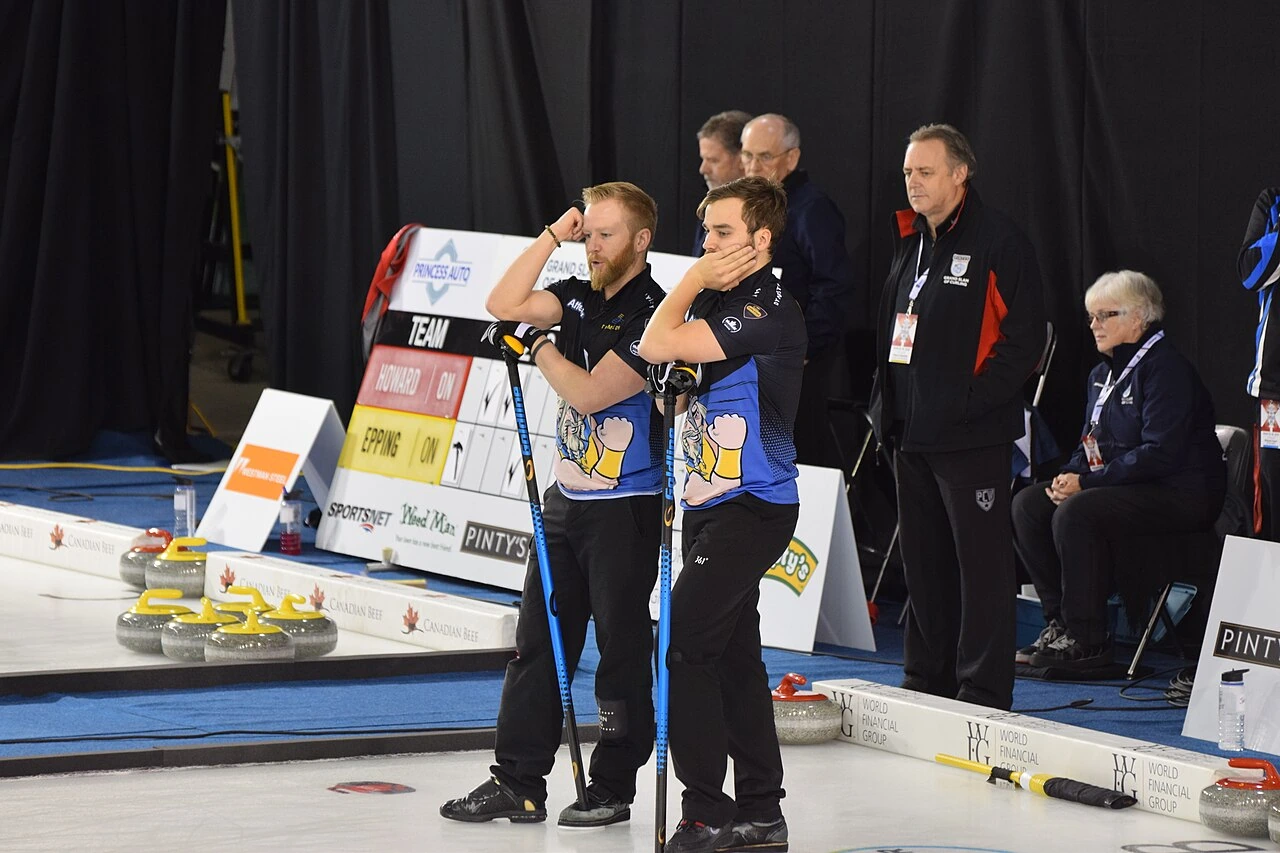 Two curling players standing on the ice during a match, one resembling Niklas Edin in the foreground.