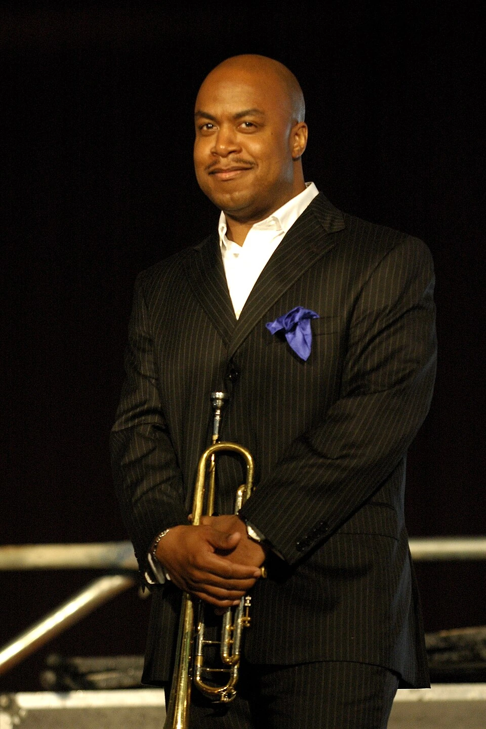 Nicholas Payton holding a trumpet on stage in a formal suit