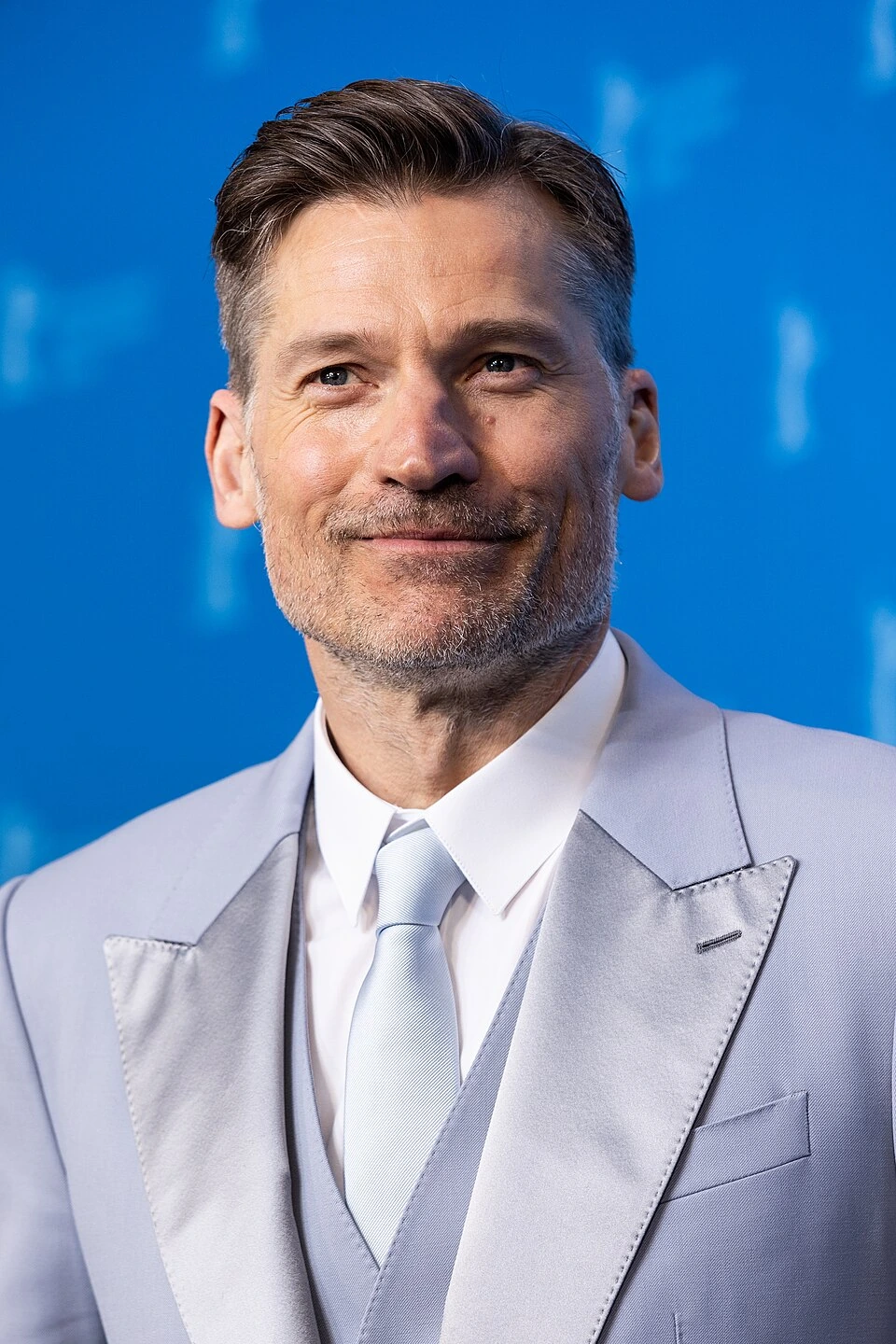 Nikolaj Coster-Waldau at a public event in a light suit against a blue background
