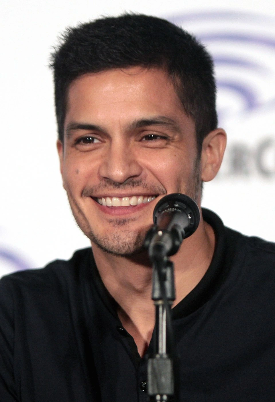 Nicholas Gonzalez speaking at a microphone, smiling in a close-up event photo.