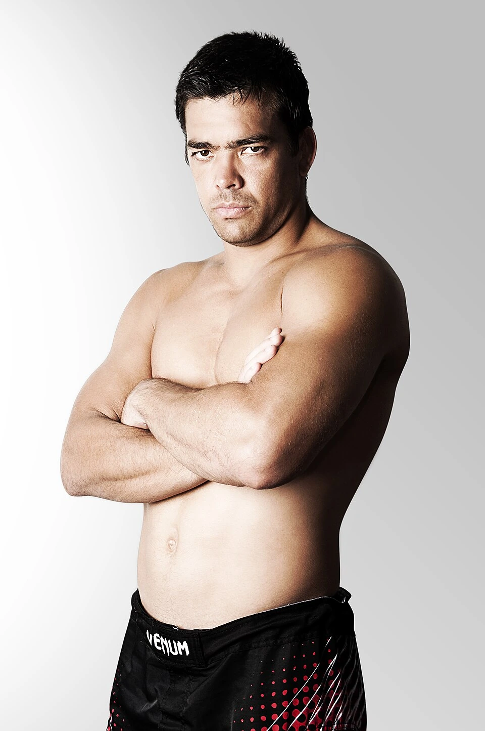 Lyoto Machida posing shirtless with arms crossed against a plain studio background