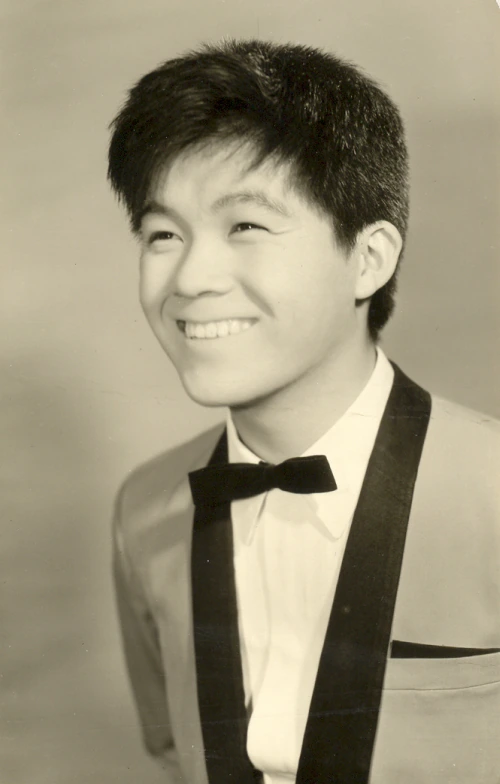 Kyu Sakamoto in a vintage portrait photo, smiling in a suit and bow tie.