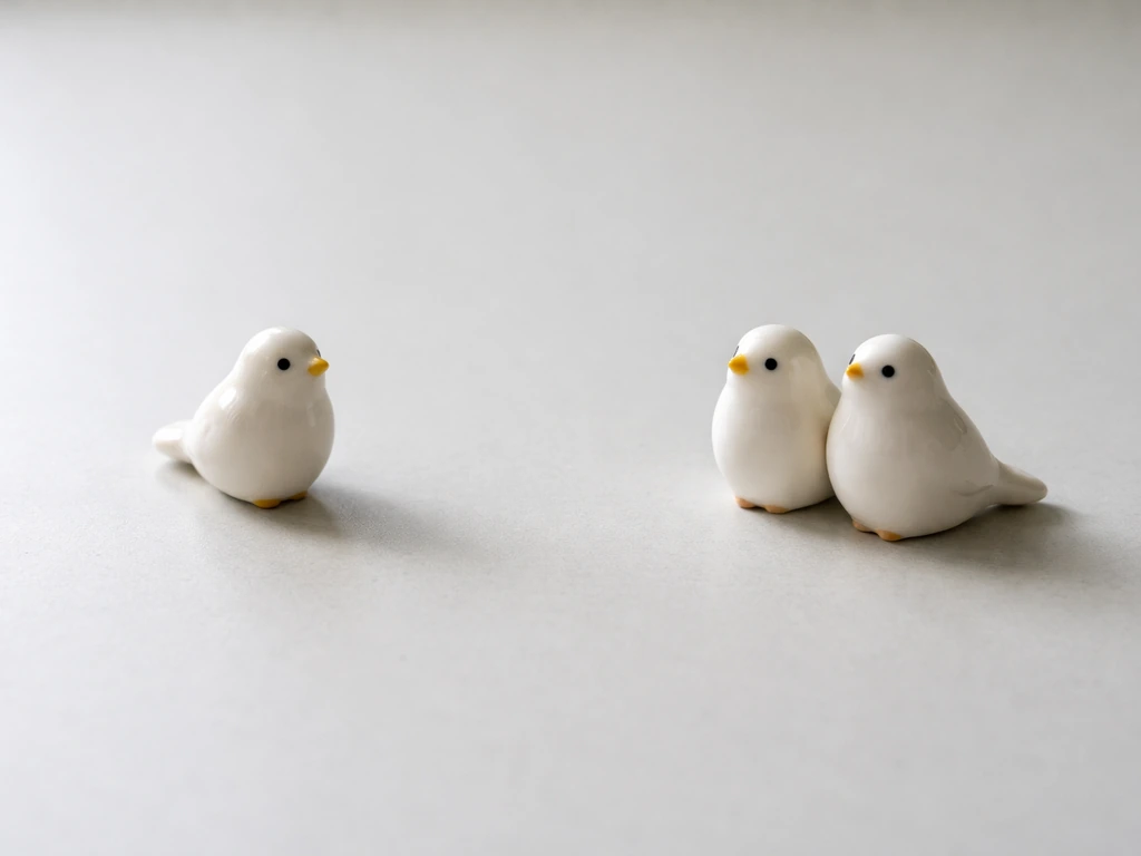 Two bird figurines showing one vs two birds on a plain tabletop