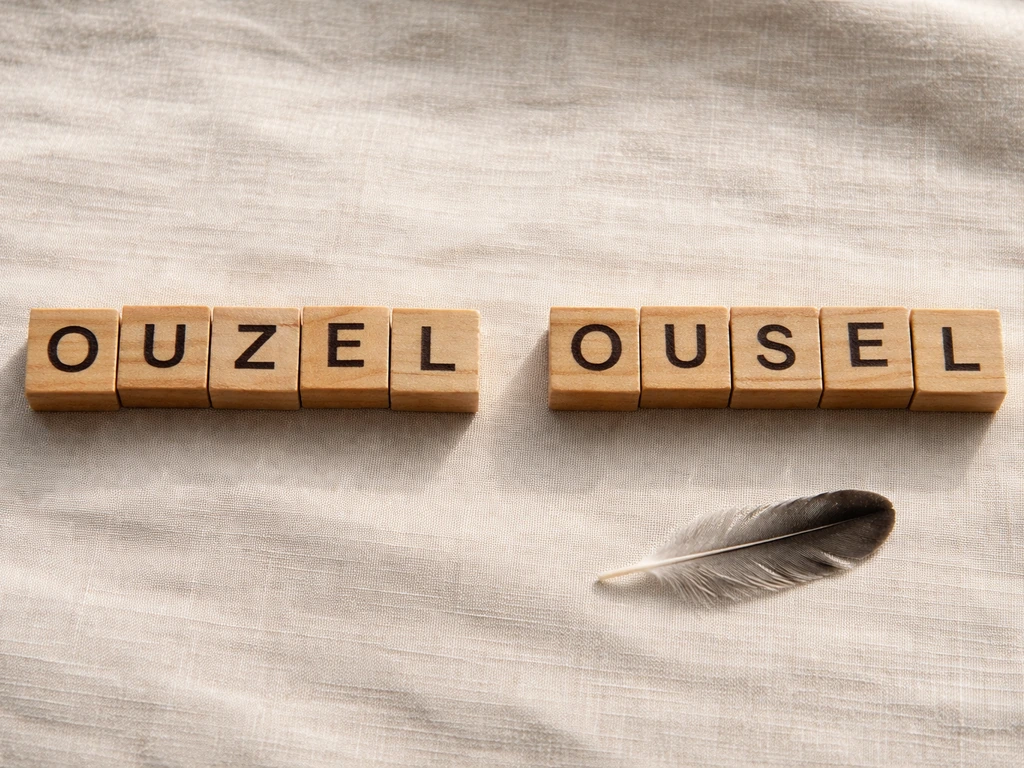 Side-by-side wooden letter tiles showing OUZEL and OUSEL with a small feather on linen fabric.