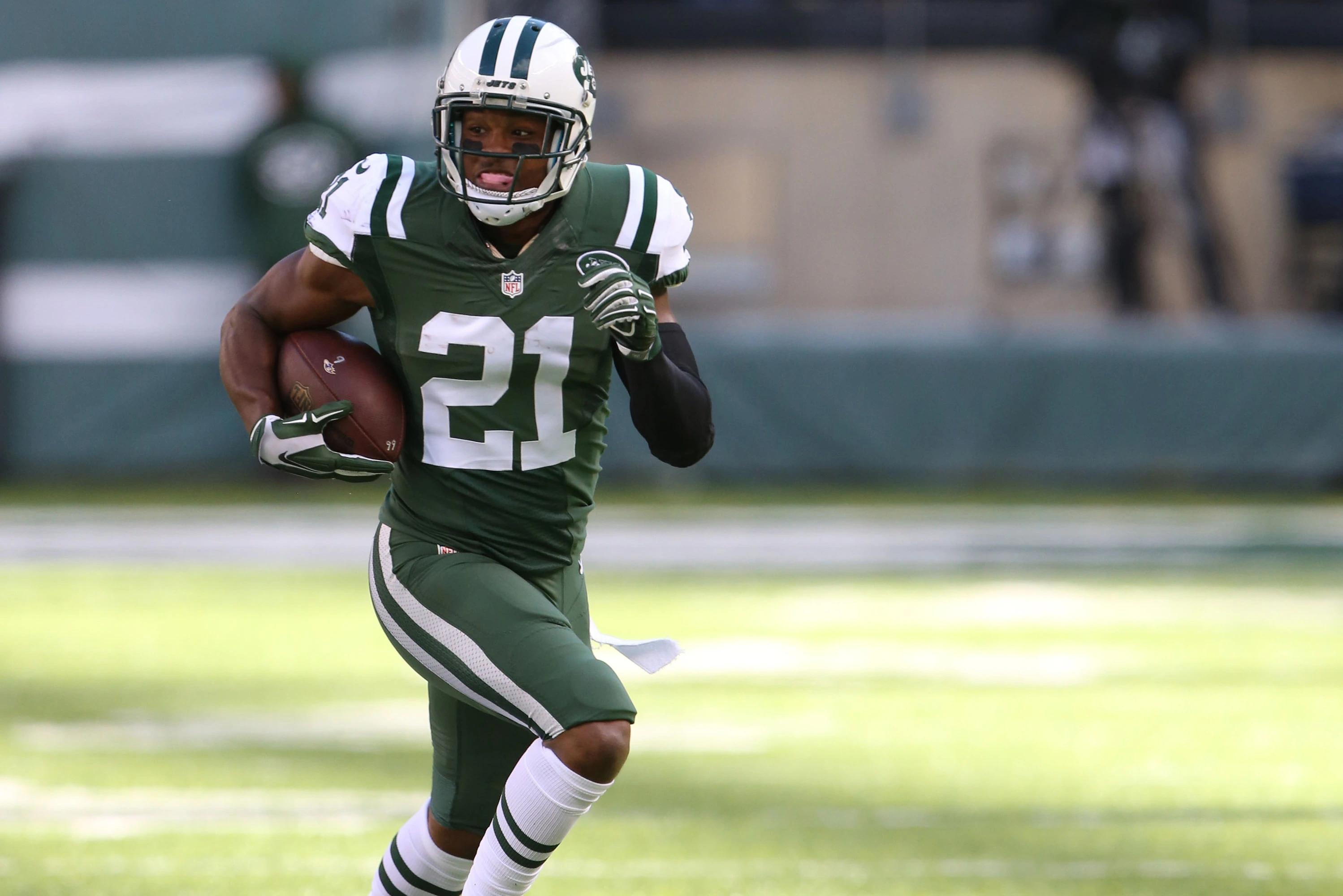 Marcus Gilchrist running in a New York Jets uniform during a game or practice, carrying the football and looking ahead.
