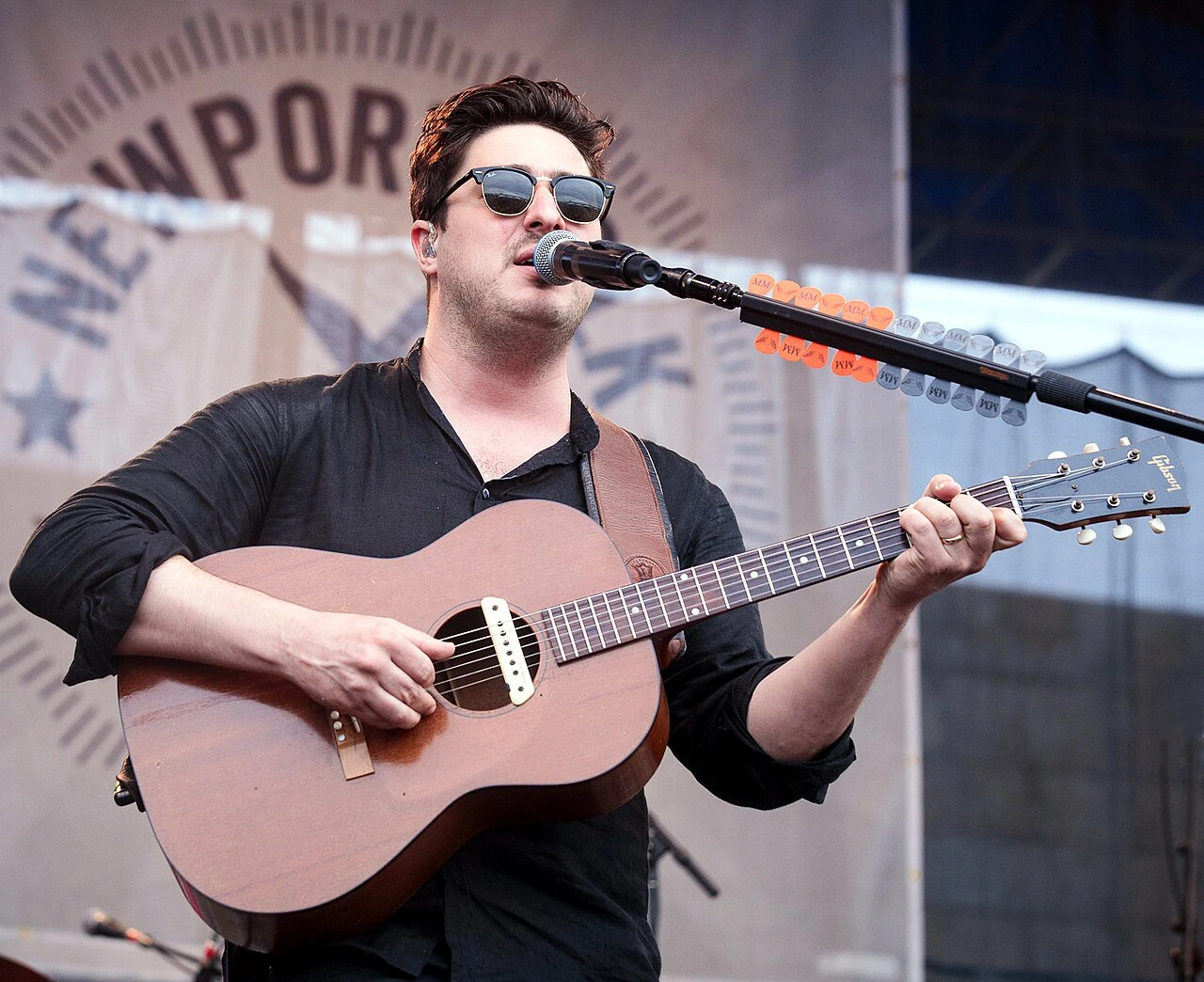 Marcus Mumford performing at the Newport Folk Festival in 2018, singing and playing acoustic guitar.