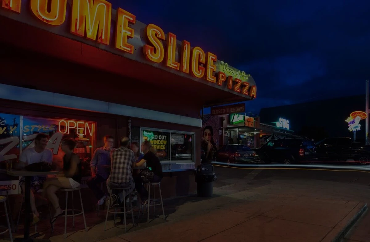 Exterior of Homeslice Pizza at night with neon signage and patio seating