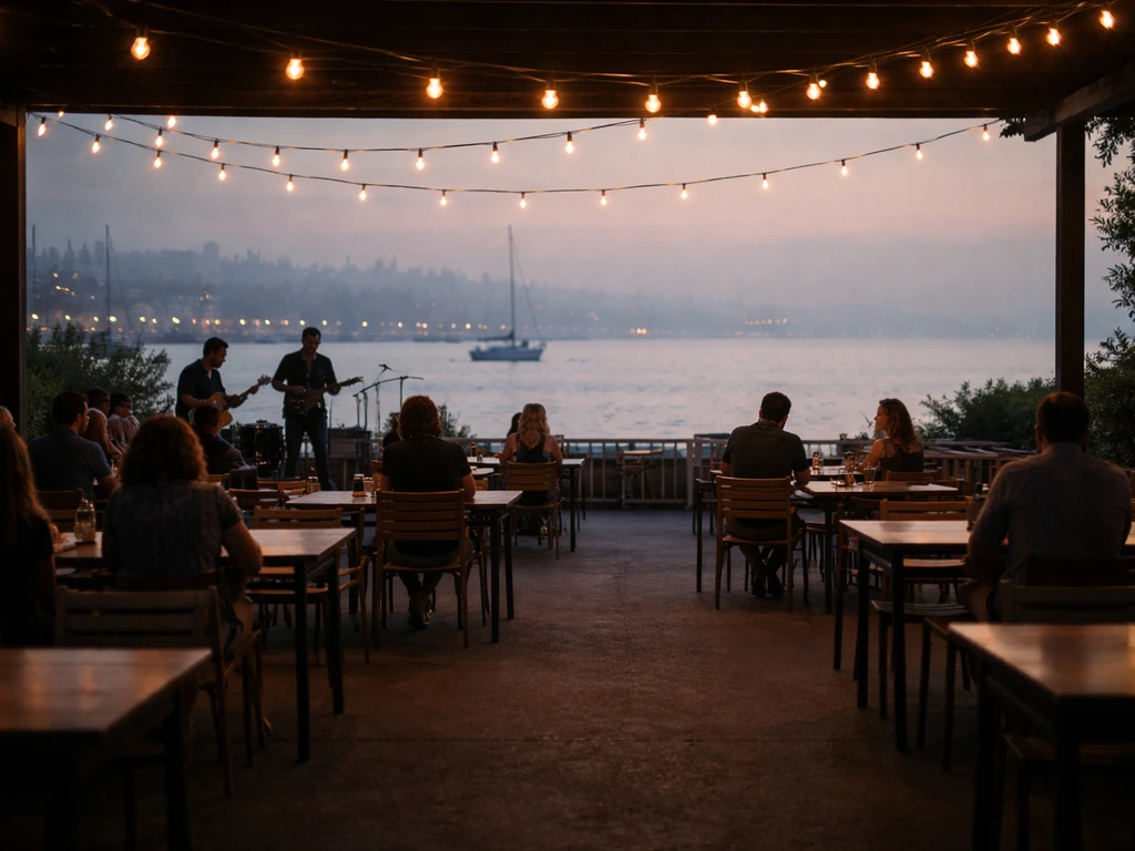 Wide waterfront patio with warm lights and a distant live band, guests seated, bay view in the background.
