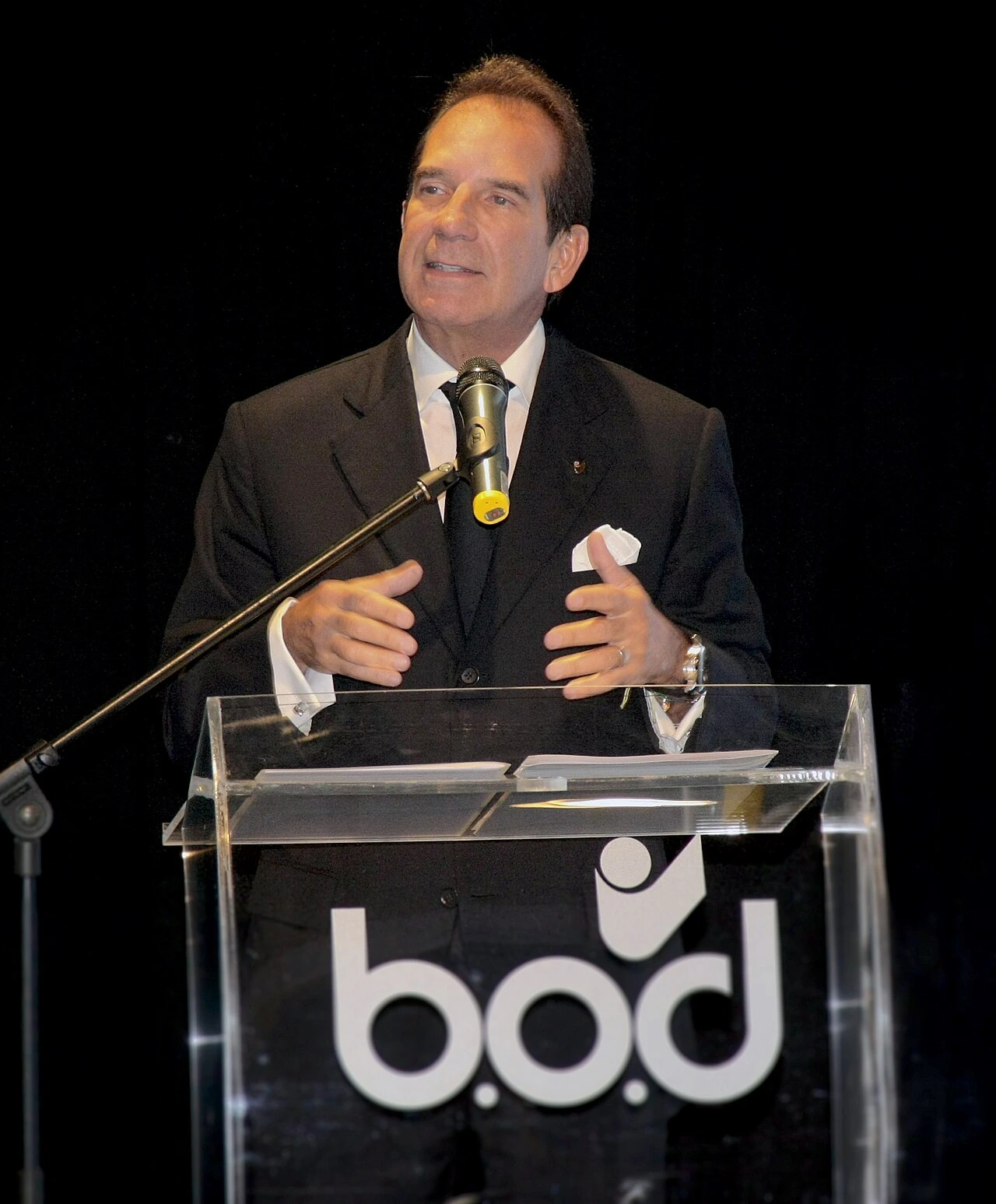 Víctor Vargas speaking at a podium during an event, in a suit and tie.