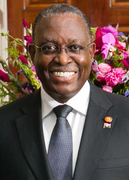 Manuel Vicente smiling in a suit and tie in front of flowers