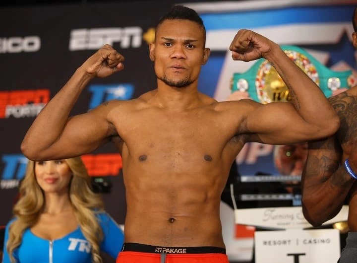 Victor Alvarez posing on stage at a boxing weigh-in, flexing both arms against a promotional backdrop