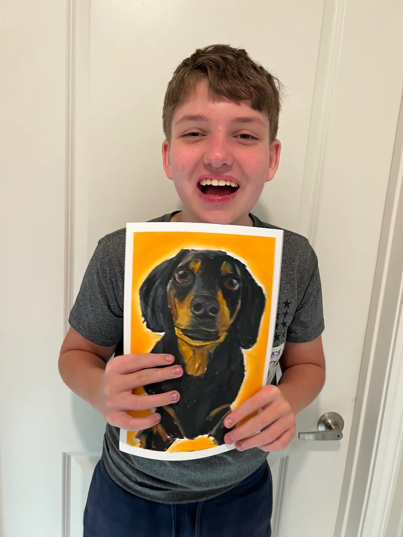 Teen artist smiling while holding a painted portrait of a dog