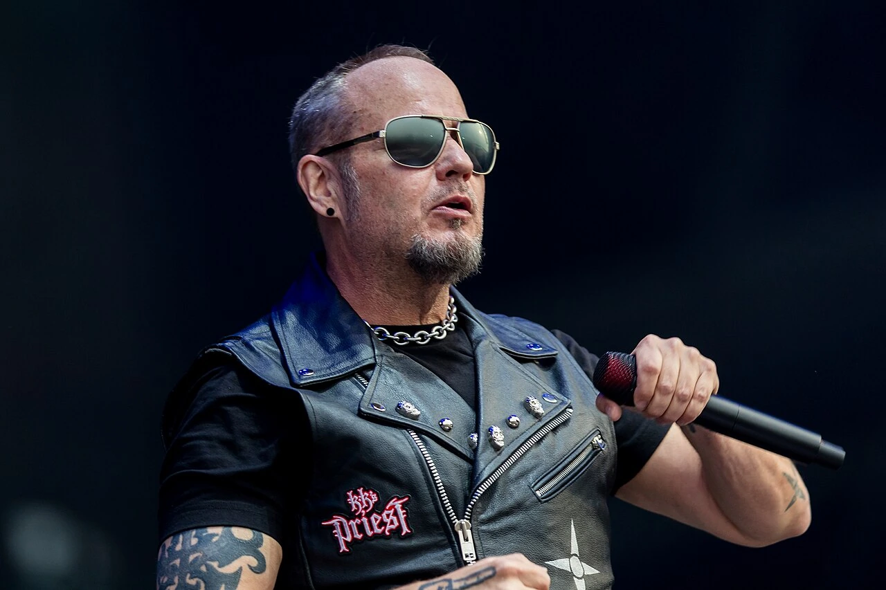 Tim "Ripper" Owens performing live with KK's Priest on stage, holding a microphone and wearing sunglasses and a black le