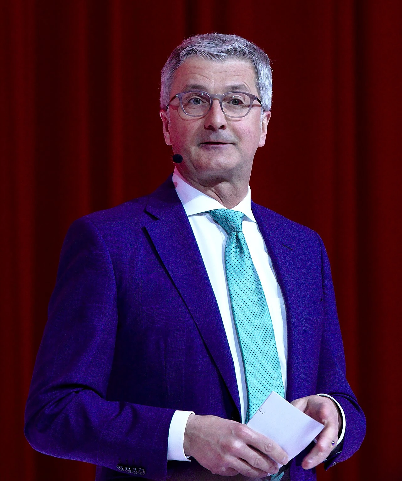 Rupert Stadler speaking on stage in a suit and tie.