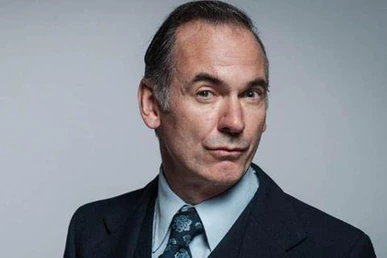 Portrait of British actor Paul Ritter in a suit against a plain background