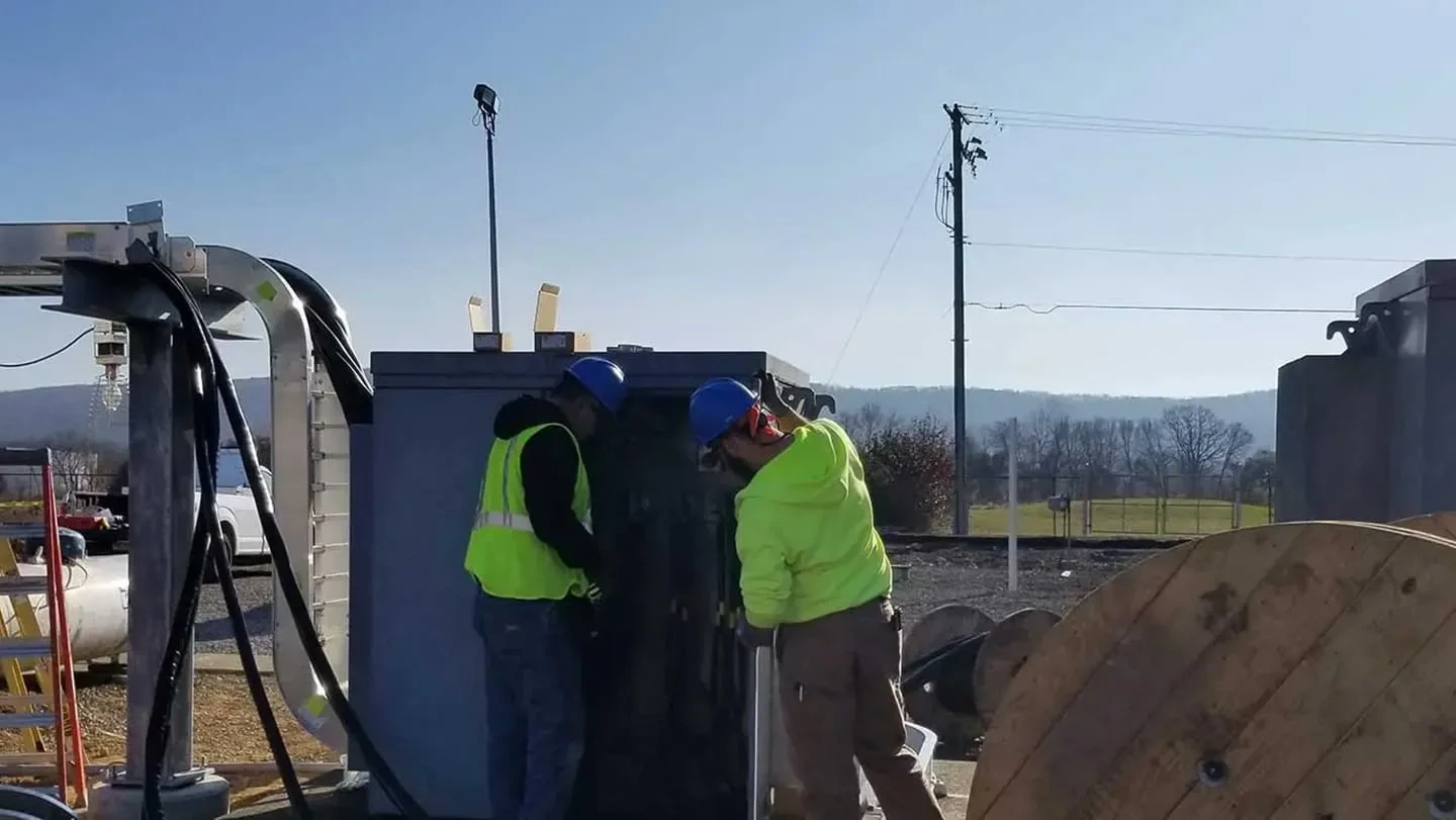 Construction workers in safety gear working on utility infrastructure equipment at an outdoor job site