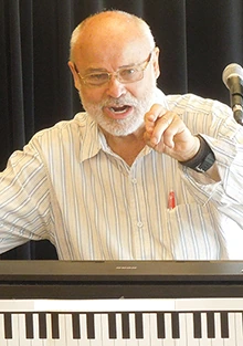 Seth Riggs speaking at a summer vocal workshop in Varberg, Sweden, standing behind a keyboard and gesturing while addres