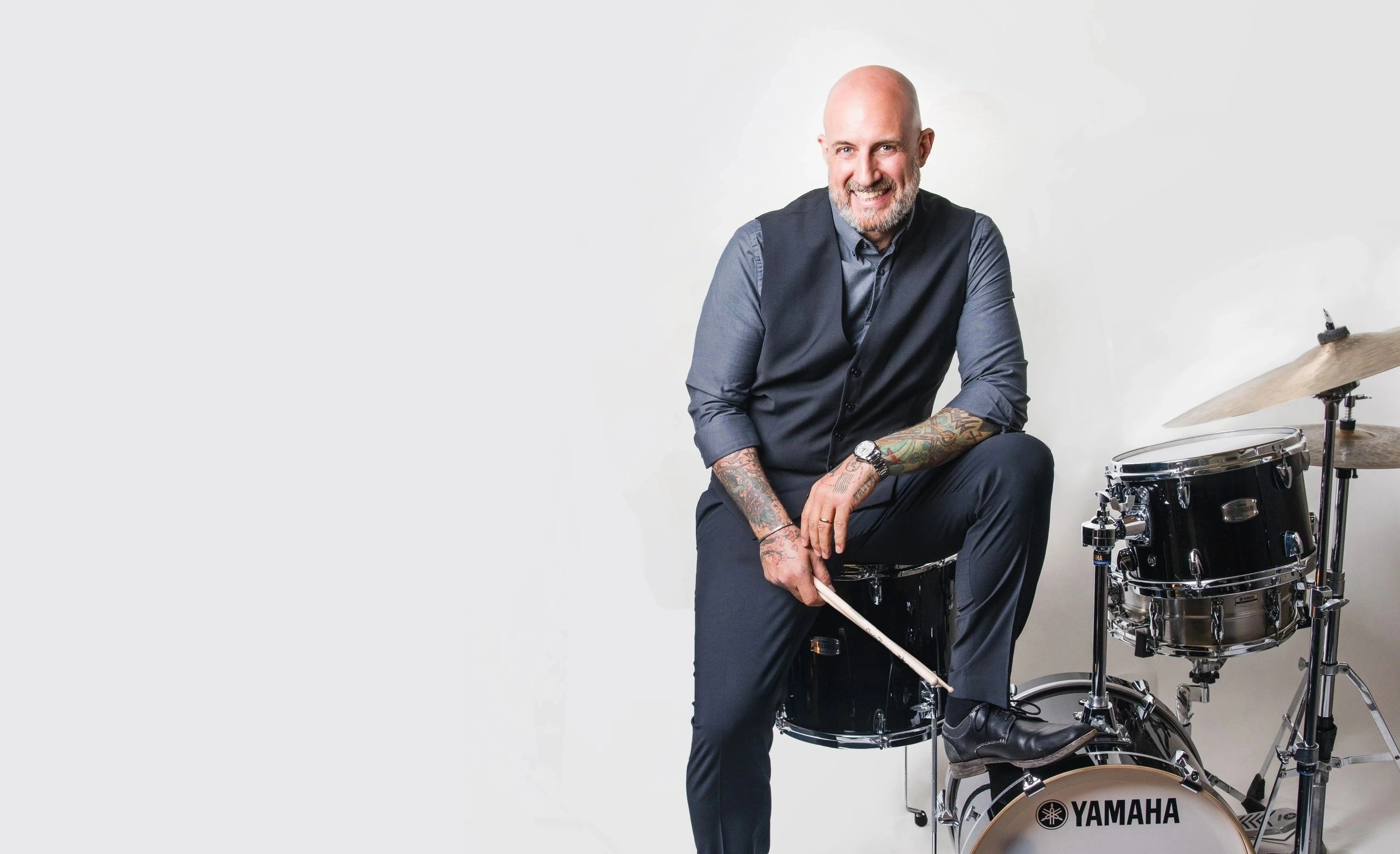 Chris Ruggiero seated on a drum kit in a studio portrait, smiling at the camera.