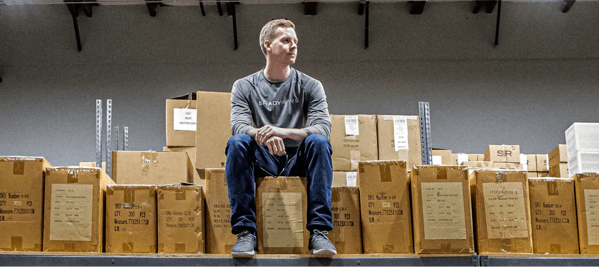 Chris Ratterman, founder and CEO of Shady Rays, seated among boxes in a warehouse