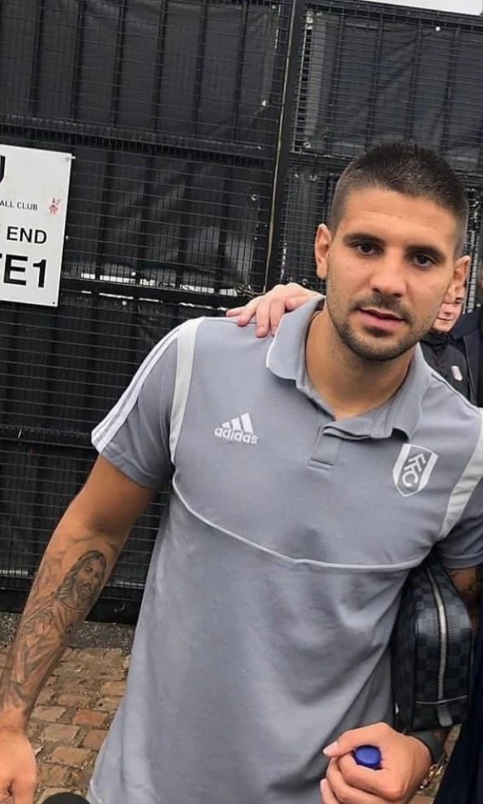 Aleksandar Mitrović posing for a photo in a grey polo shirt outside a football venue.