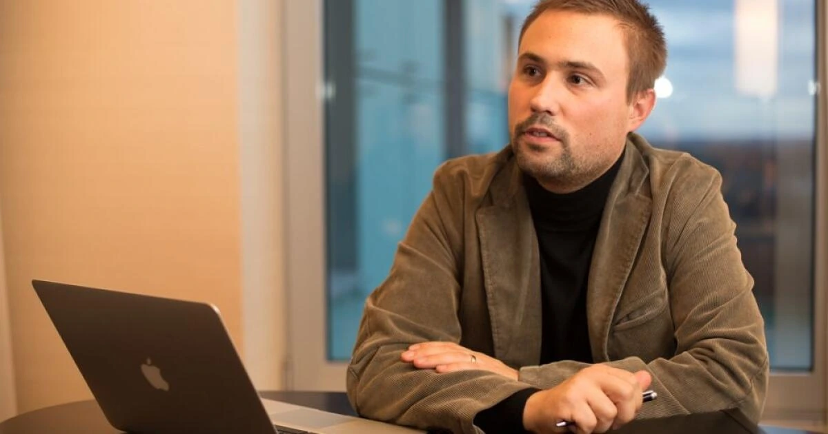 Milan Dubeč seated at a table in an office with a laptop, looking off to the side