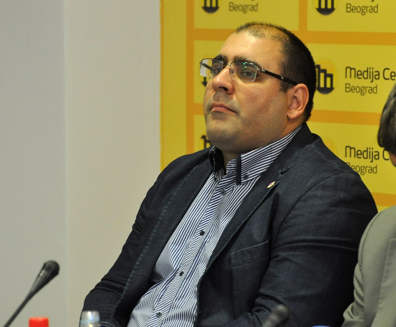 Portrait photo of Vladimir Đukanović at an event, seated indoors in front of a yellow backdrop.