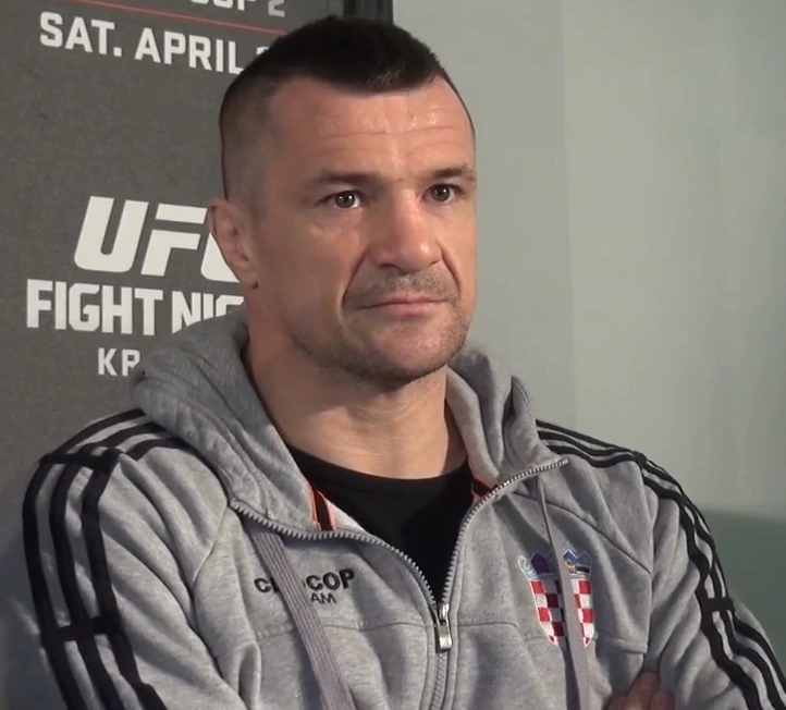 Mirko Filipović (Cro Cop) in a gray hoodie at a UFC event backdrop, shown in a candid portrait photo.