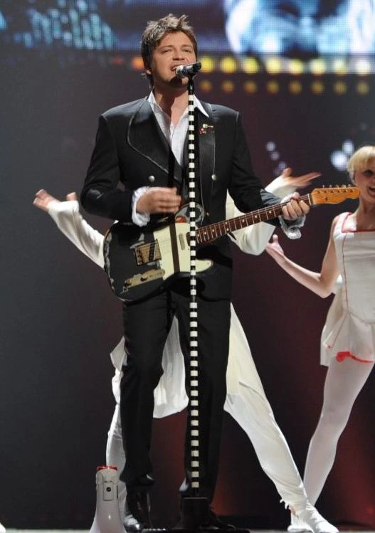 Vlatko Ilievski performing on stage with a guitar and microphone