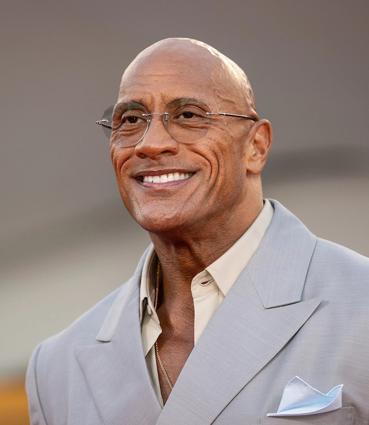 Dwayne Johnson smiling in a light gray suit at a public event
