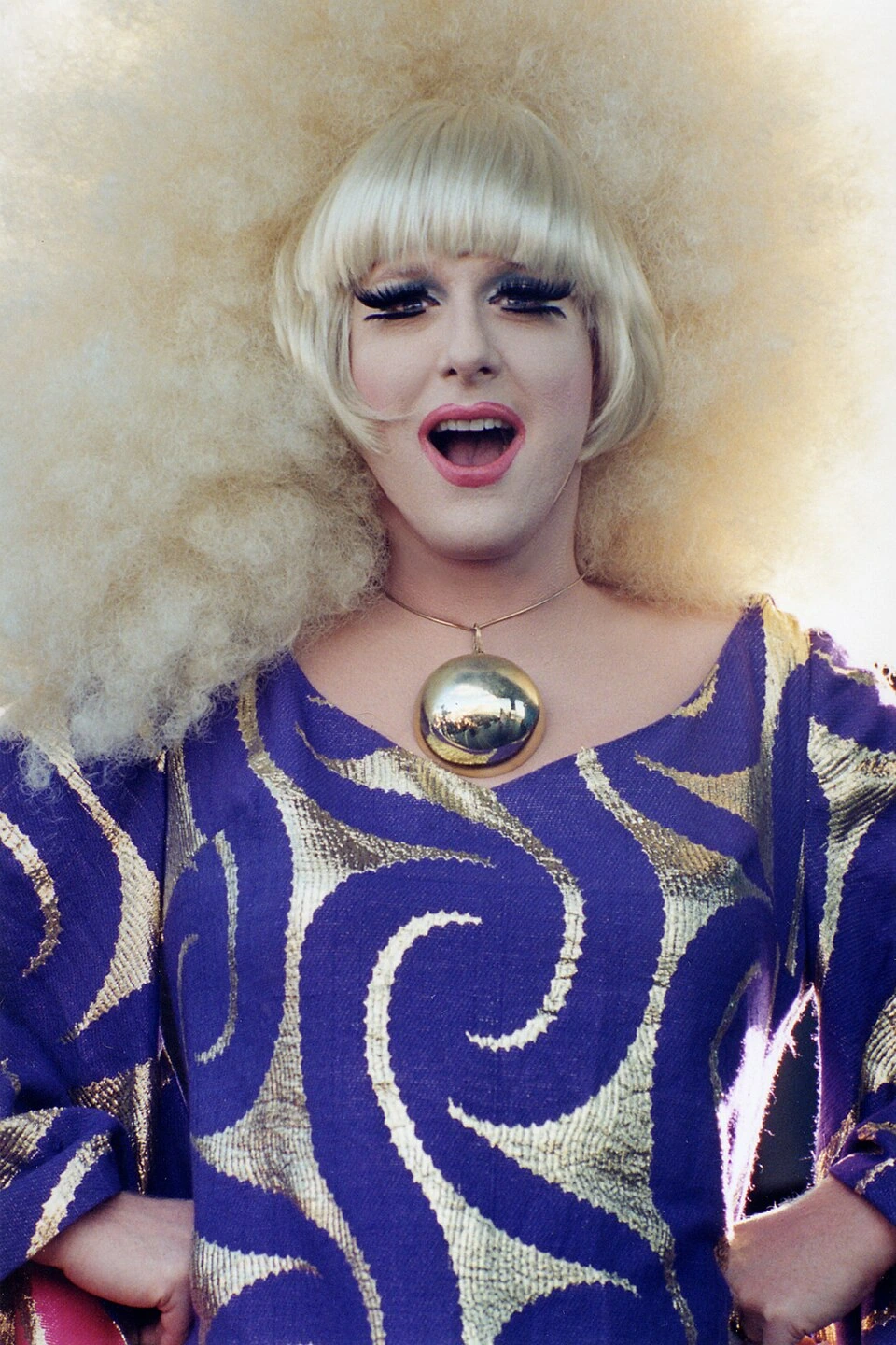 Lady Bunny posing in drag with a platinum blonde wig and bold purple patterned outfit