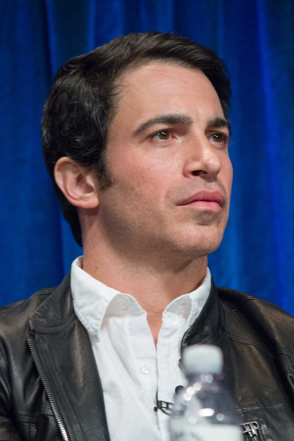 Chris Messina at PaleyFest 2013, seated in front of a blue curtain wearing a leather jacket and white shirt.