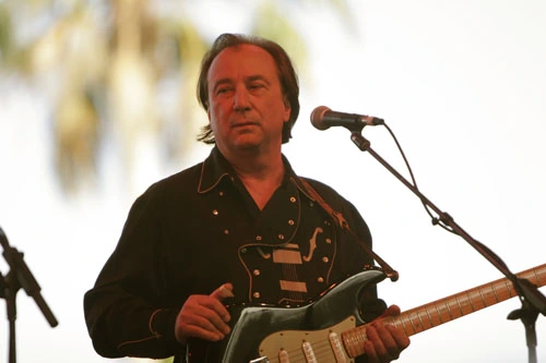 Jim Messina performing on stage with a guitar near a microphone