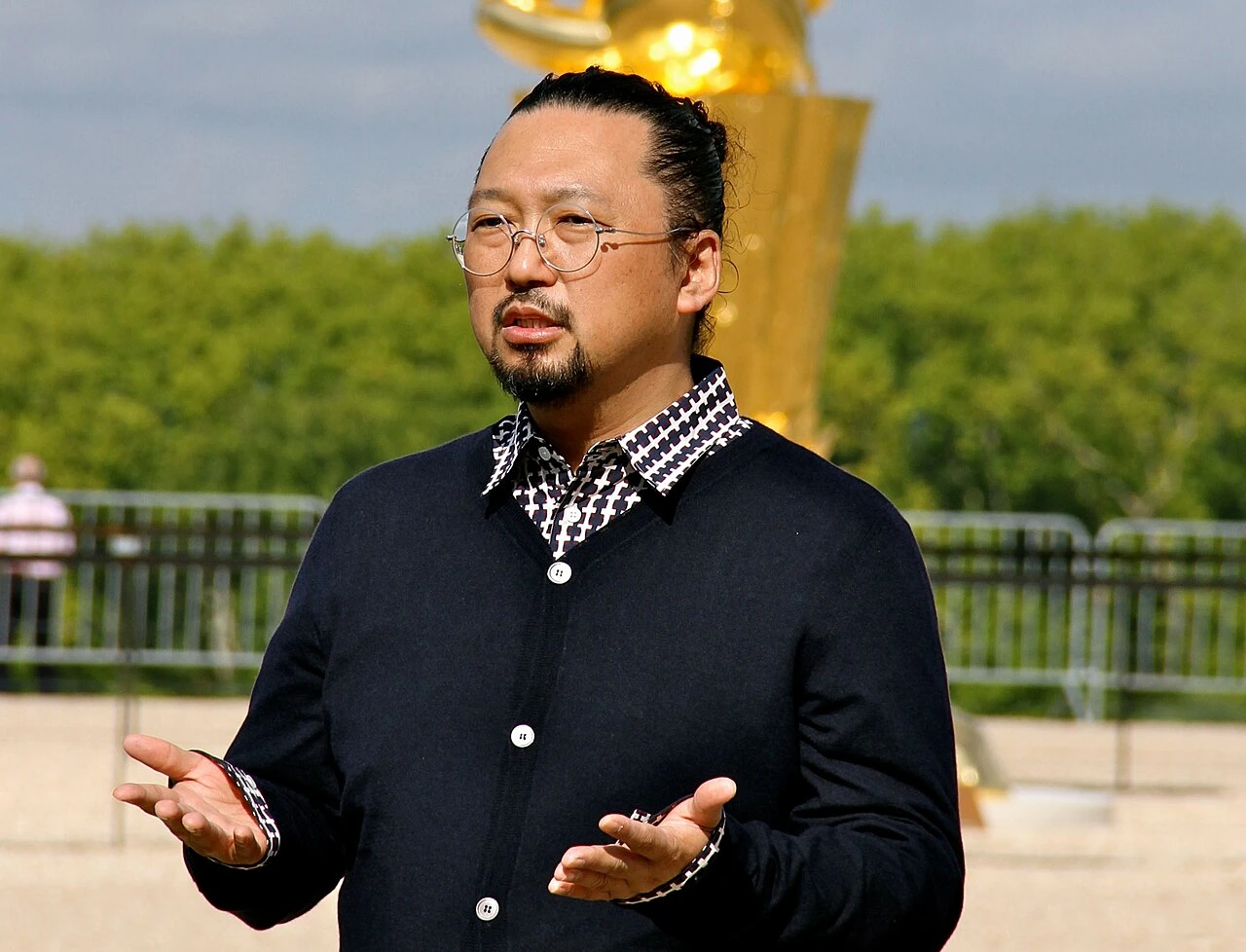 Takashi Murakami standing outdoors at Versailles, gesturing while speaking
