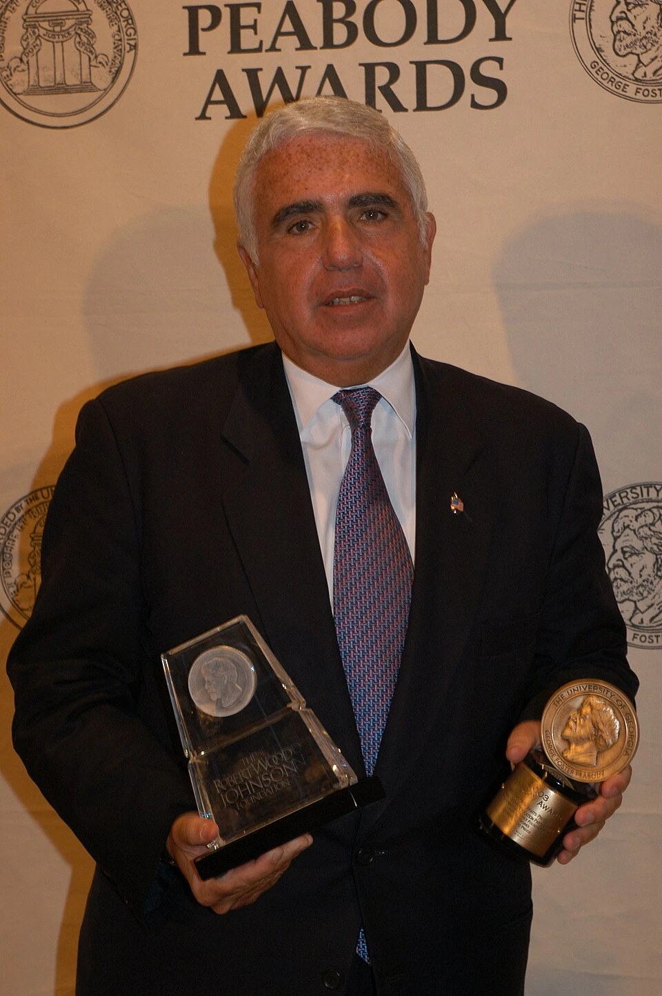 Mel Karmazin posing in a suit at an awards event holding trophies