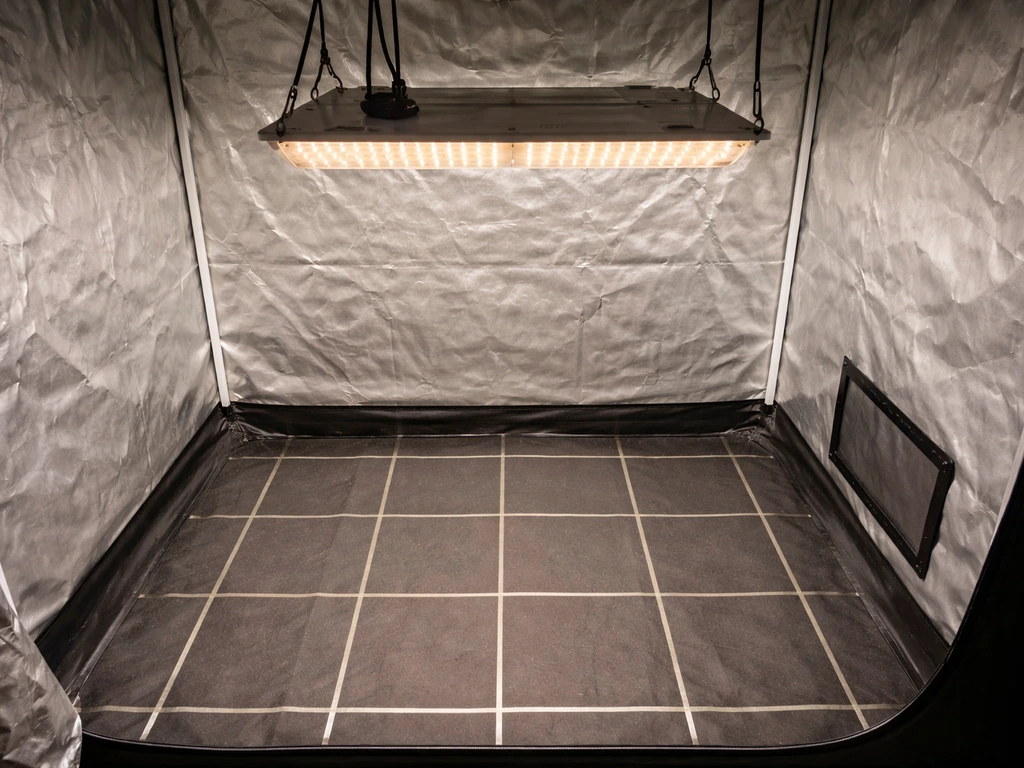 LED grow light hanging inside a grow tent with a simple coverage map grid marked on the floor