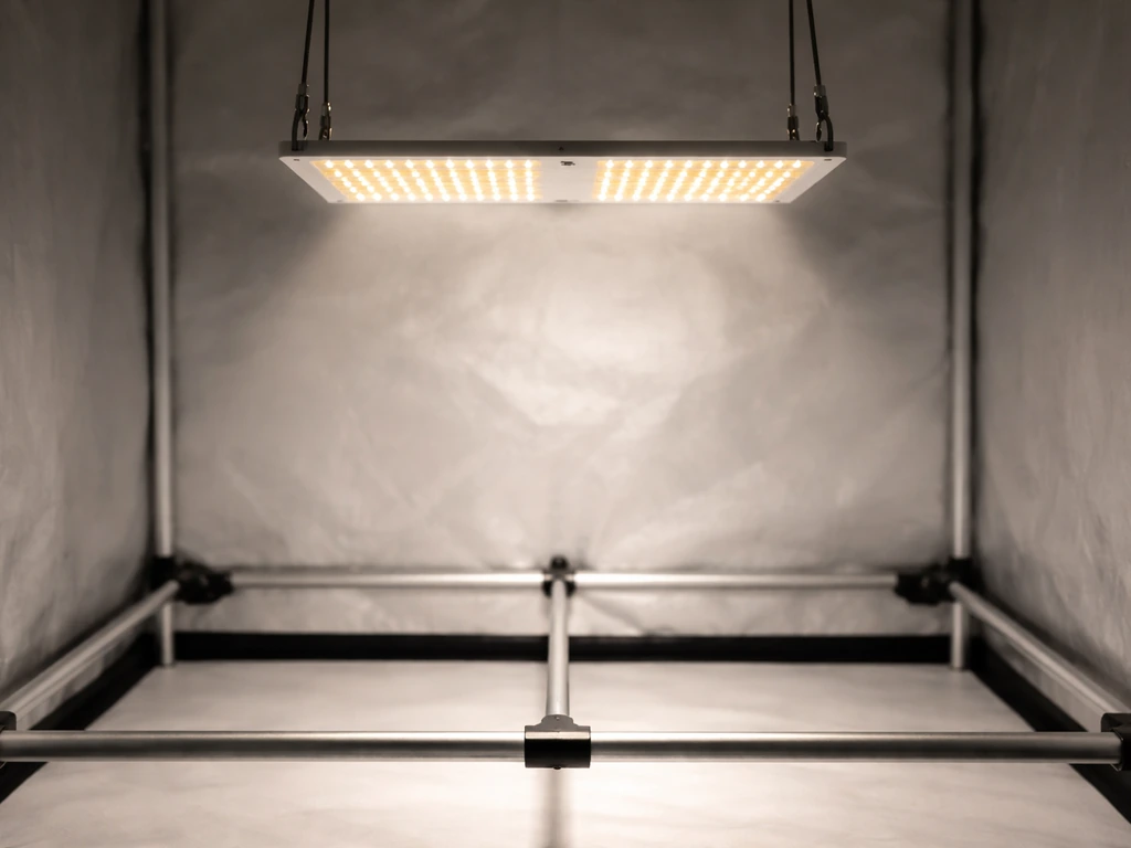 Close-up of a compact LED grow light hanging above a small 2x2 grow tent canopy inside a quiet setup.