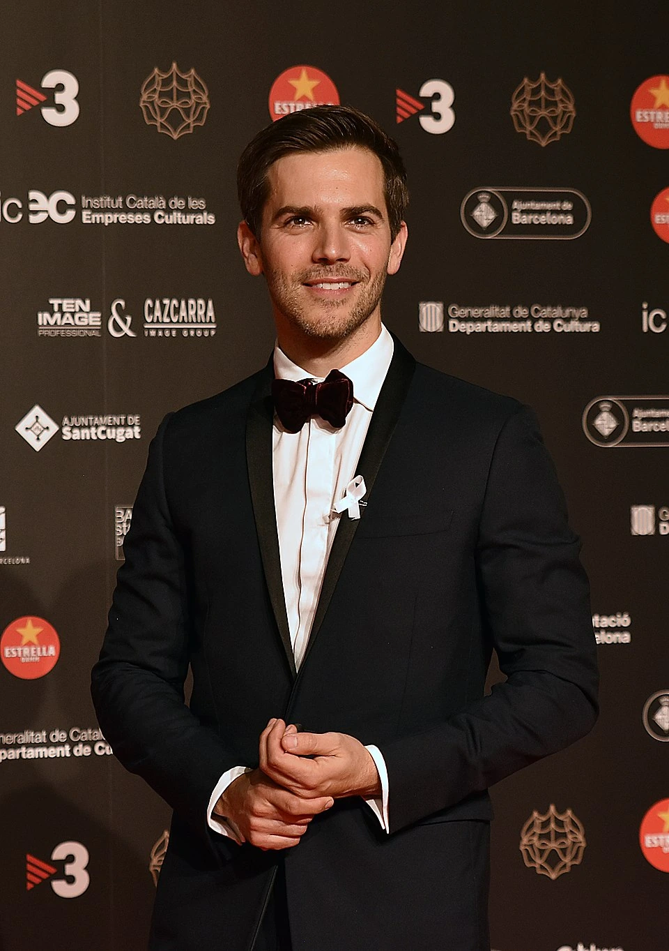 Marc Clotet posing at a formal event in a tuxedo, smiling in front of a step-and-repeat backdrop.