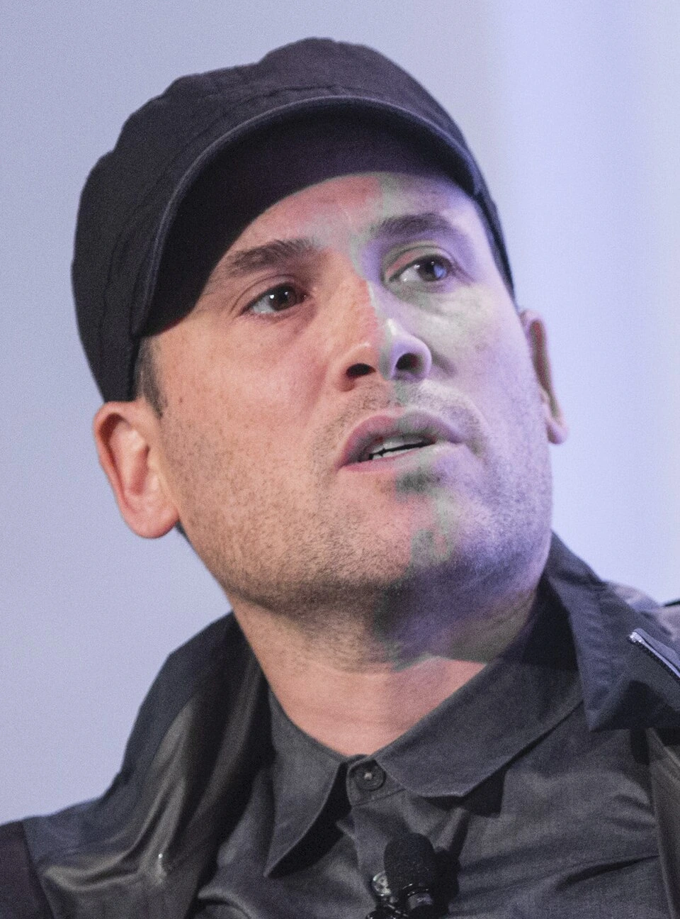 Marc Ecko in a close-up editorial portrait wearing a black cap and dark shirt