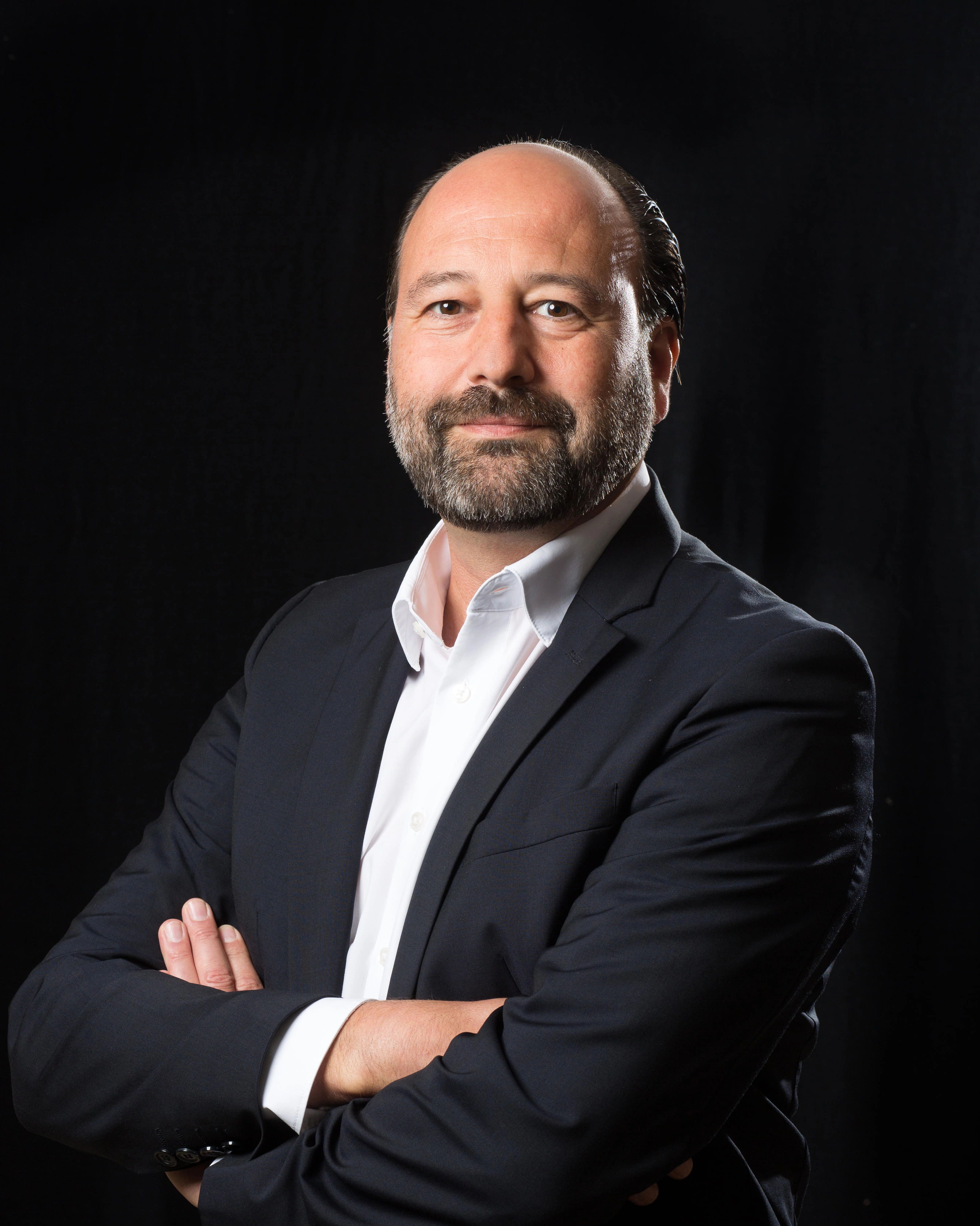 Portrait of Marc Gebauer in a dark suit against a black background