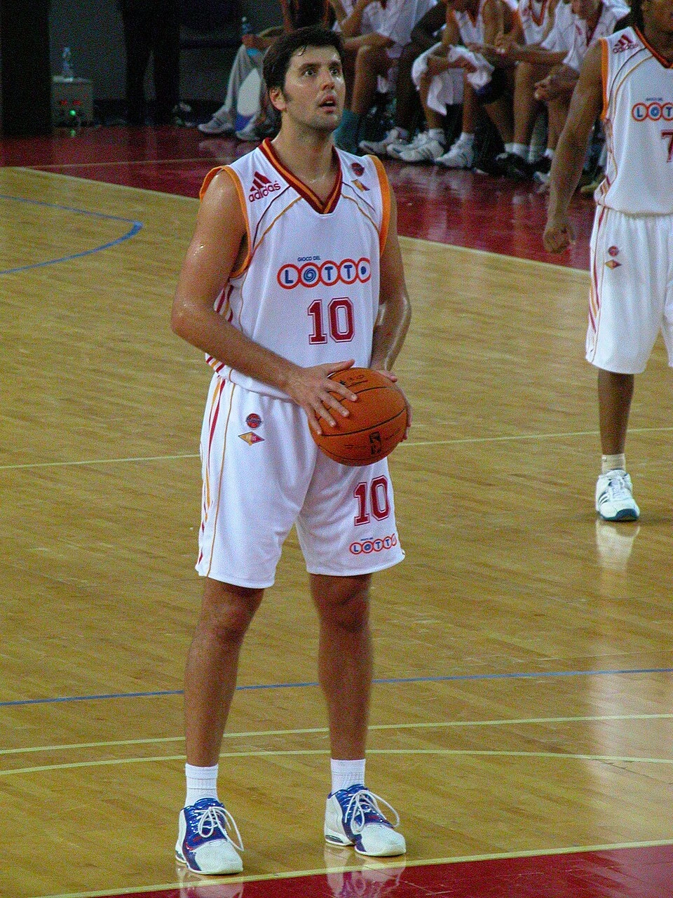 Dejan Bodiroga standing on a basketball court in a white jersey holding a basketball.