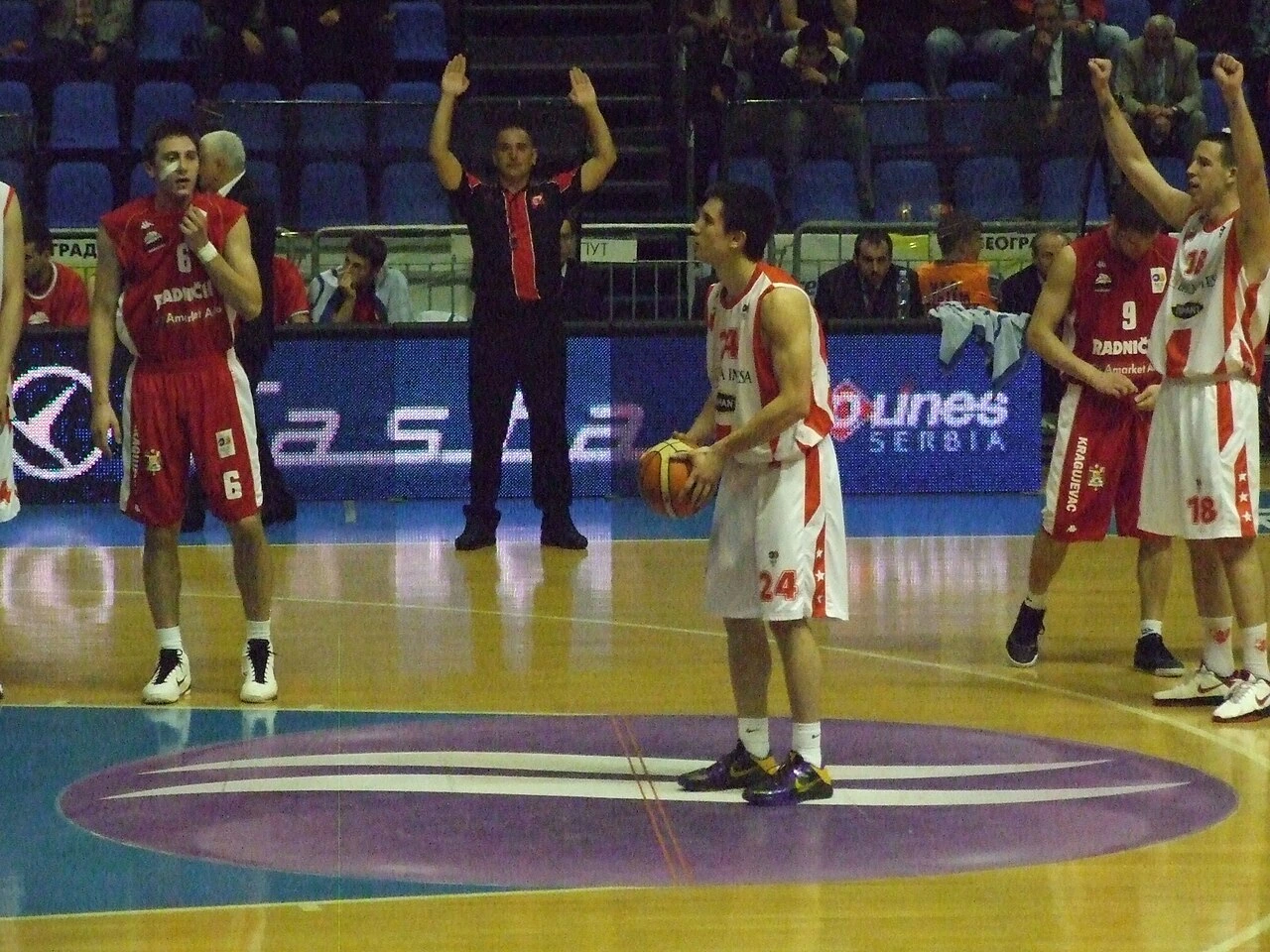 Basketball player Strahinja Stojačić standing on the court during a game in a white and orange uniform, holding the ball