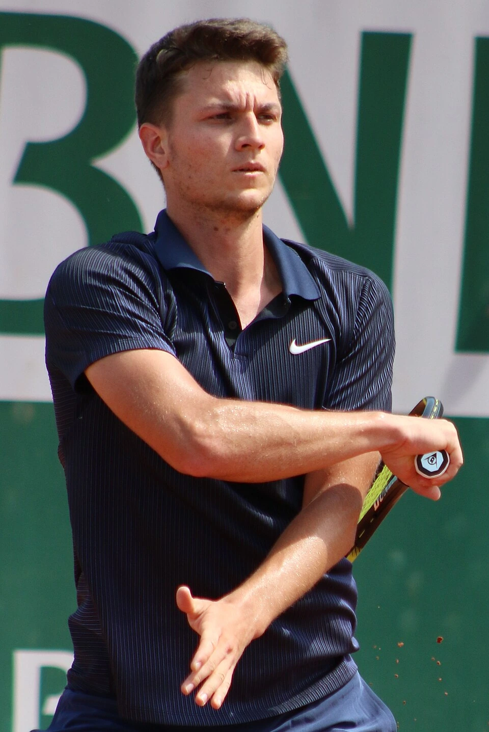 Miomir Kecmanović playing tennis in a match, wearing a dark Nike shirt and holding his racket during a forehand motion.