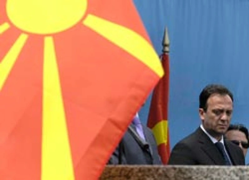 Sašo Mijalkov speaking at a podium, partially obscured by a Macedonian flag